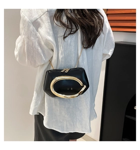 Detail of a black leather crossbody bag with a large gold metal handle and chain strap