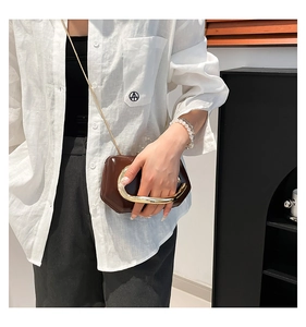 Detail of dark brown glossy leather handbag featuring a large circular gold metal handle