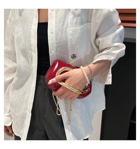 Detail of red patent leather handbag featuring a thick gold metallic handle and chain strap