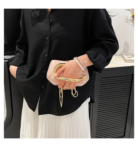 Close-up of pink patent leather clutch featuring bold gold U-shaped handle and chain