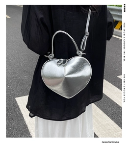 Street style shot of a silver heart-shaped crossbody bag worn over the shoulder