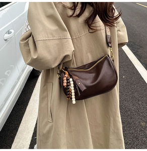 Detail of vintage coffee leather crescent bag with bohemian beaded tassel and woven strap