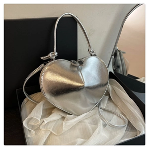 Detail view of silver heart crossbody bag with mirror finish on white silk in a gift box