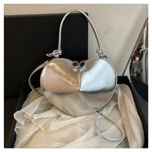 Close-up of silver heart-shaped crossbody bag with dual zipper and glossy mirror finish