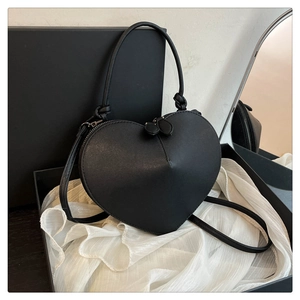 Detail of a black heart-shaped leather crossbody bag with dual leaf zippers on silk cloth