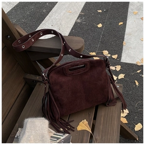 Detail einer burgunderroten Wildledertasche mit Fransen und Gurt auf Herbstbank