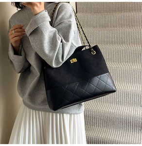 Detail of a black quilted tote bag featuring a gold twist lock and a woven chain strap