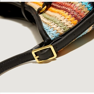Close-up of colorful woven straw bag with black leather straps and gold metal buckles