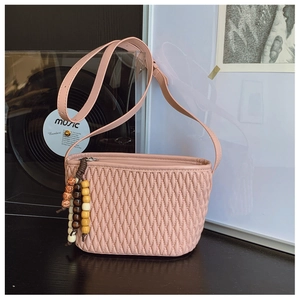 Detail of pink quilted crossbody bag with ethnic style wooden bead charm and long strap