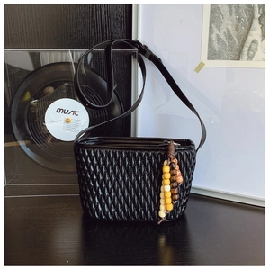 Detail of black pleated shoulder bag featuring glossy texture and beaded tassel charm