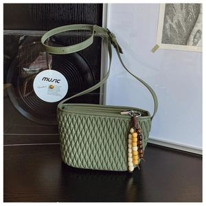 Macro detail of dark green pleated faux leather crossbody bag with wooden bead charm