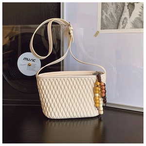 Detailed view of cream quilted bucket bag featuring a wooden bead tassel and smooth PU leather
