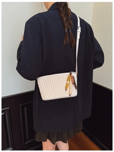 Detail of a beige quilted pleated bag with decorative beaded tassel and chain strap
