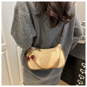 Detail der beigen Hobo-Tasche mit rotem Kirschanhänger und braunem Rand an der Schultertasche