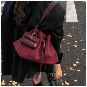 Detail of burgundy suede drawstring bucket bag with leather pouch on a street background