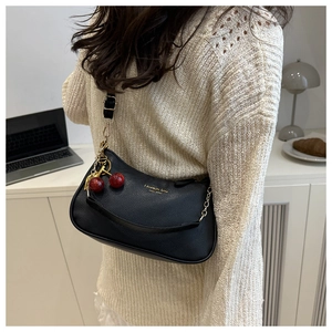 Detail of black lychee texture shoulder bag with red cherry charm and chain strap