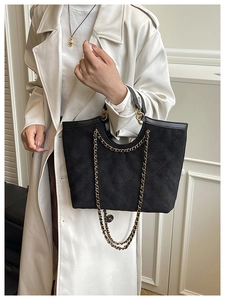Détail d'un sac cabas matelassé noir avec bandoulière chaîne sur un manteau
