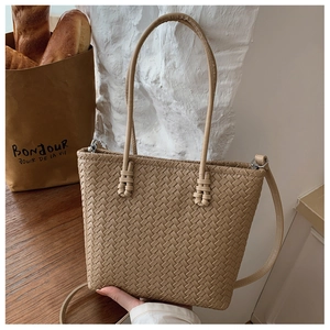 Detail of khaki woven tote bag showing texture, dual handles and long shoulder strap