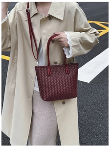 Detailed close-up of dark red woven leather bucket bag with top handles and shoulder strap
