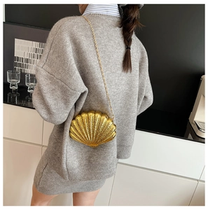 Golden shell-shaped evening clutch bag with metal chain strap shown on model shoulder
