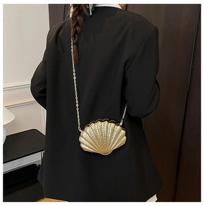 Golden shell-shaped evening bag with metallic texture and thin chain strap on a model