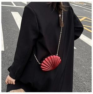 Detail of burgundy shell-shaped crossbody bag with grain texture and gold chain strap