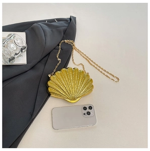 Detailed shot of a gold shell clutch bag with chain strap and phone for scale
