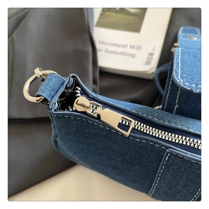 Dettaglio della cerniera in metallo argentato e cuciture bianche sulla borsa di jeans