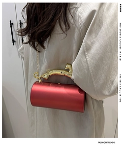 Detail of red cylindrical clutch with golden leopard handle and detachable chain strap