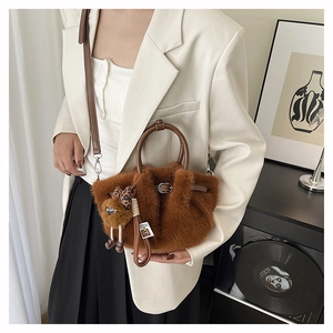 Detail van karamel faux fur handtas met lederen handvat en pluche bedeltje op een model