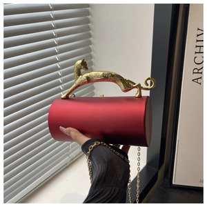 Detail of red cylindrical evening clutch featuring a gold leopard handle and chain