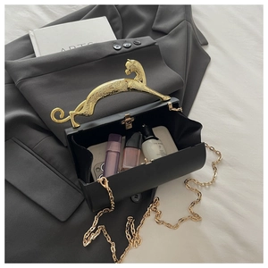 Detail of black acrylic box clutch featuring a golden leopard handle and metal chain