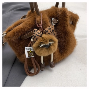 Close-up of brown faux fur bucket bag with leather handles and cute plush charm