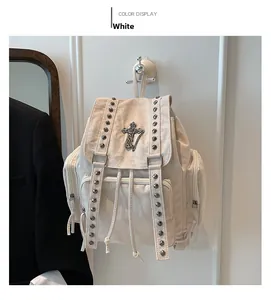 Detail eines weißen Canvas-Rucksacks mit silbernen Nieten und Kreuzanhänger im Goth-Stil