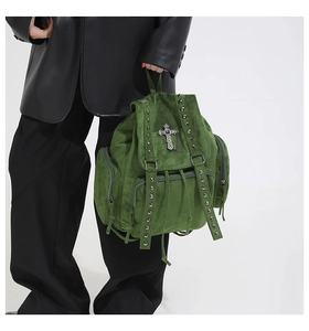 Detail eines dunkelgrünen Samt-Rucksacks mit Metallnieten und silbernem Kreuzanhänger