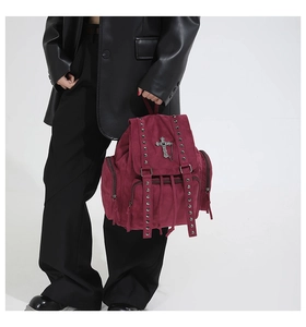 Detail eines gotischen weinroten Rucksacks mit Metallkreuz-Anhänger und Nietendekor