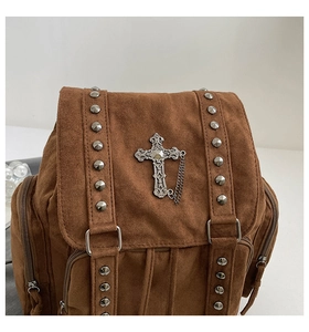 Detail eines silbernen Kreuz-Emblems mit Ketten und Nieten auf braunem Wildlederrucksack