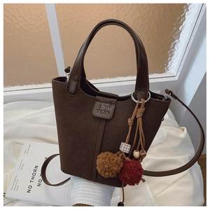 Dettaglio della borsa a secchiello marrone scuro con ciondoli di peluche e texture in pelle