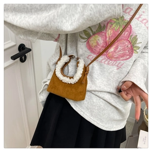 Detail of a brown suede dumpling bag with white faux shearling trim and slim strap