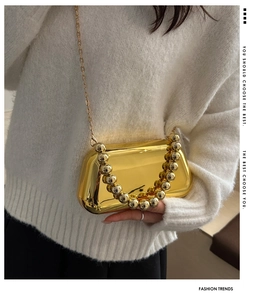 Detailed close-up of a glossy gold acrylic clutch bag with a beaded handle and metal chain