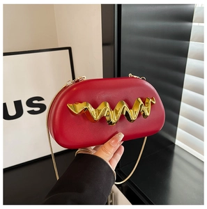Macro view of red leather evening clutch featuring a wavy gold metal buckle and snake chain