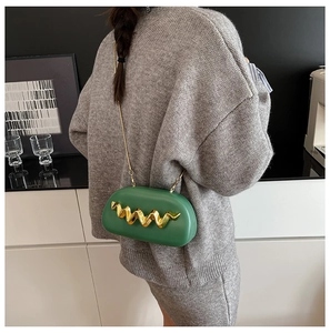 Detail of emerald green oval hardshell clutch with golden wavy metal trim and chain