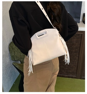Detail showing side tassels and adjustable strap on a cream PU tote bag
