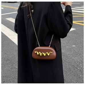 Brown capsule crossbody bag with gold metal wave accent and slim chain strap on black coat