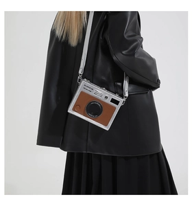 Detail shot of the camera-shaped silver crossbody bag worn over a black leather jacket