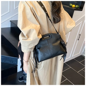 Detail of black leather tote bag with long tassels and metallic eyelet shoulder strap
