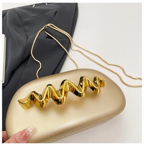 Detail view of gold hardshell clutch with wavy metal handle and snake chain strap