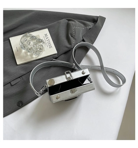 Detailed top view of a mini silver camera-shaped hardshell crossbody bag on a suit