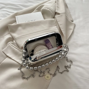 Silver metallic acrylic clutch bag with bead handle and chain strap on white blazer