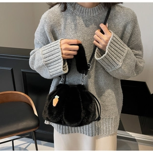 Detail of black plush bucket bag with carrot charm worn by a model in grey sweater